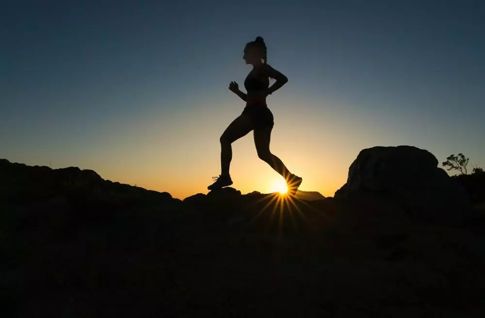 silhouette of a girl jogging in a rocky area with the sun in the background