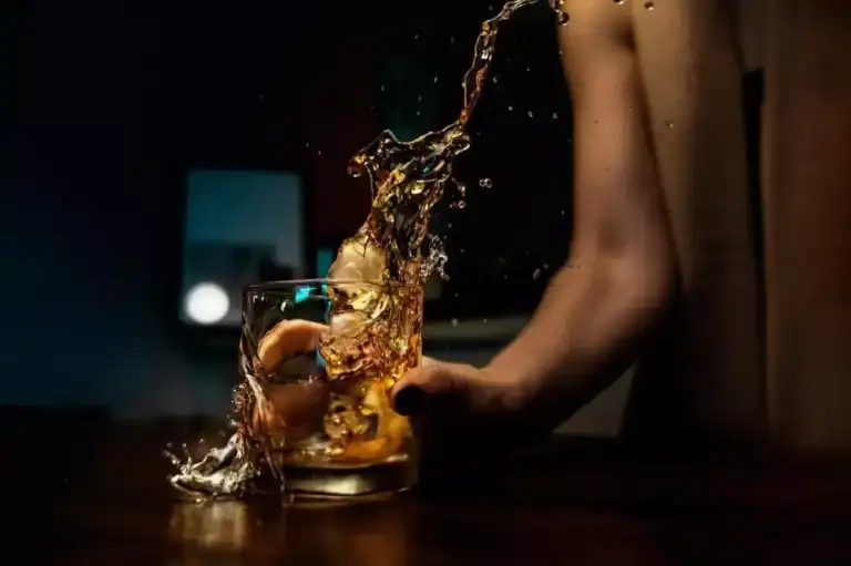 image of woman experiencing alcoholism placing a glass with an alcoholic beverage on the table roughly