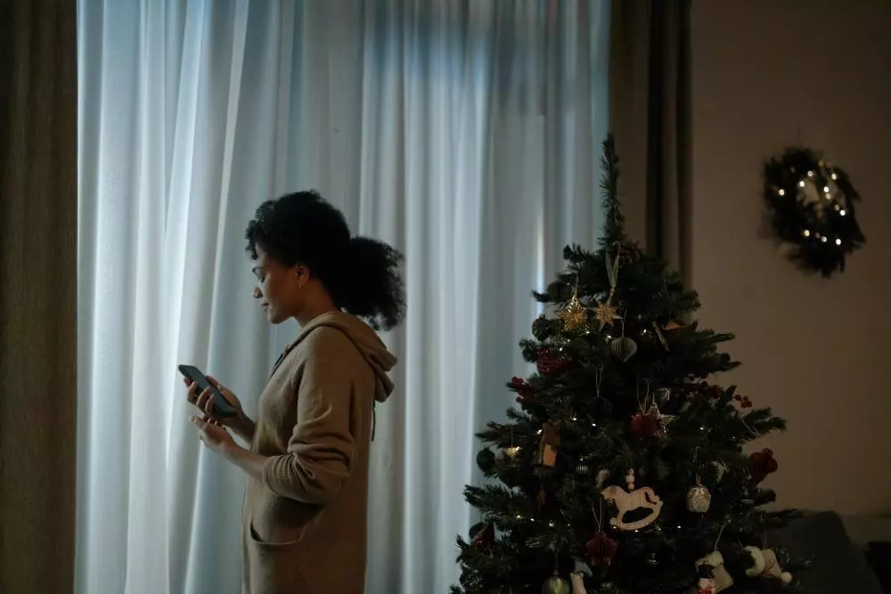 image of a woman looking at her cell phone next to the christmas tree