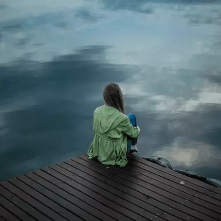image of a girl sitting alone on a dock in front of the river