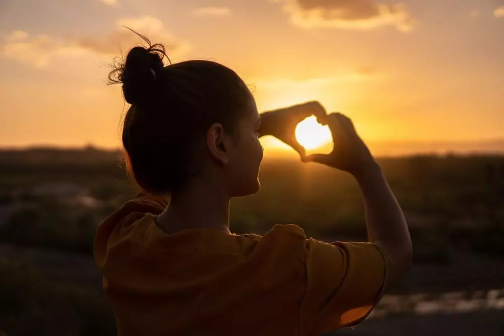 image of girl forming a heart with her hands in the direction of the sun